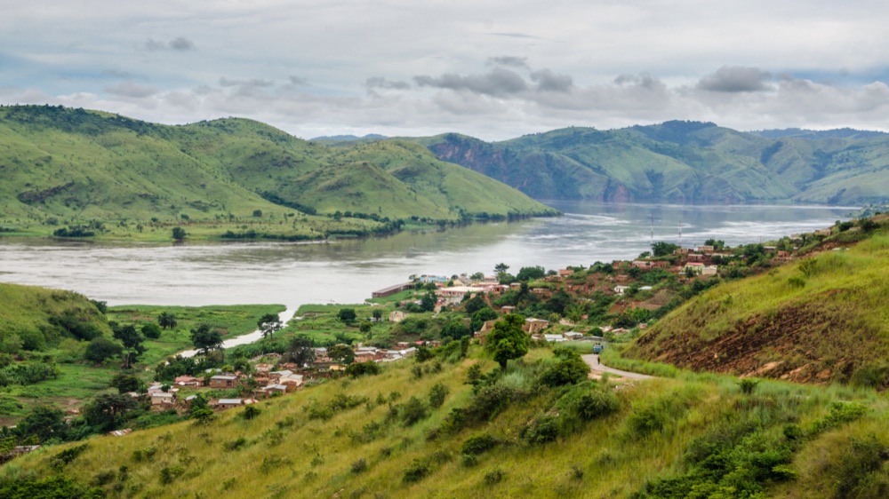 Green hills and a village along a wide river in the Democratic Republic of Congo.