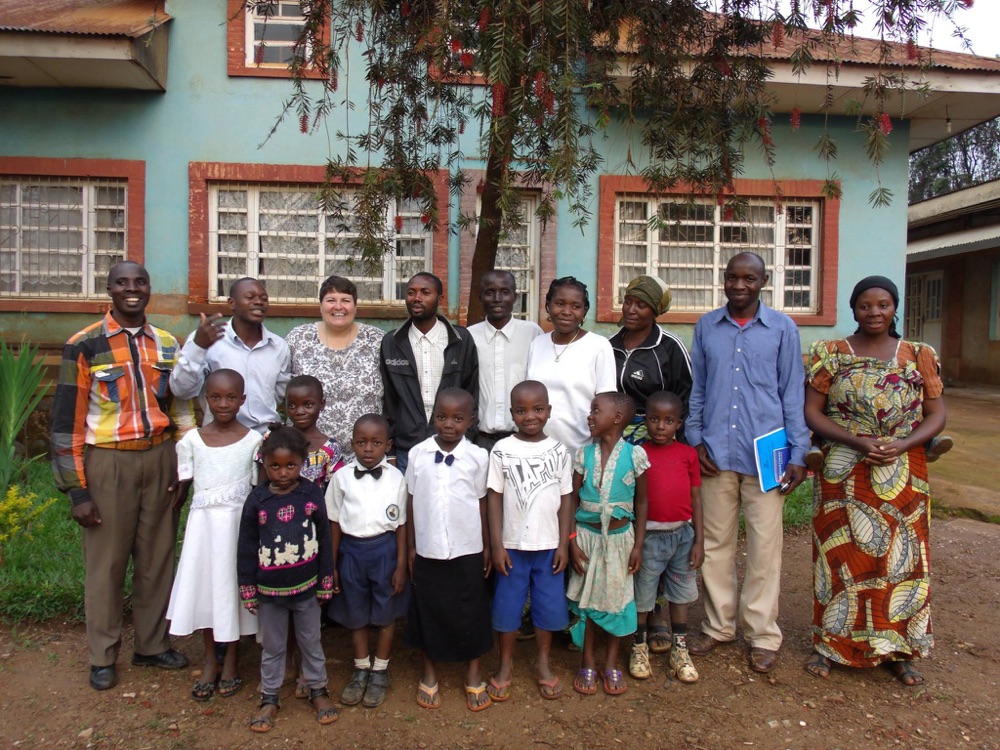 Students in their best clothes stand with teachers and a Kids in the Congo volunteer outside a school building.